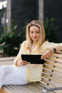 Beautiful woman sits on a bench in the summer in the city and makes online purchases using