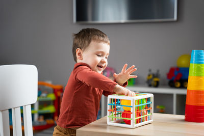 A cute little toddler boy of two years old plays with multi-colored balls and sits 