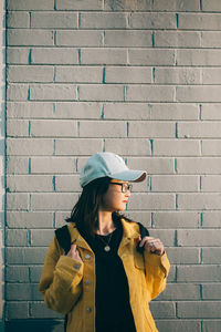 Young woman wearing hat against brick wall