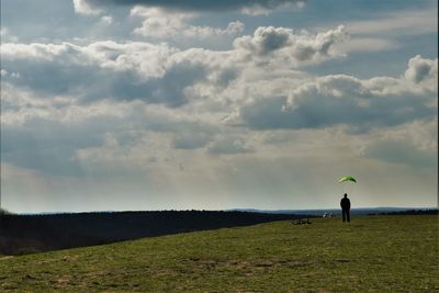 Rear view of man standing on field against cloudy sky