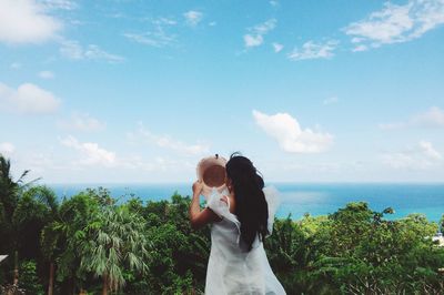 Rear view of woman standing by sea against sky