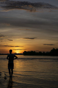 Rear view of silhouette man standing on beach against sky during sunset