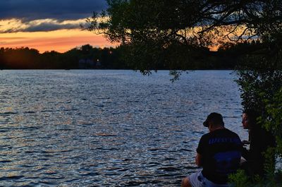 Rear view of men sitting by tree against sky during sunset