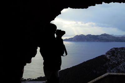 Silhouette man photographing sea against sky