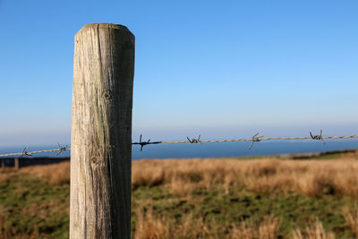 Barbed wire fence on field against clear sky