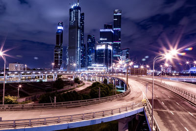 Illuminated street amidst buildings against sky at night