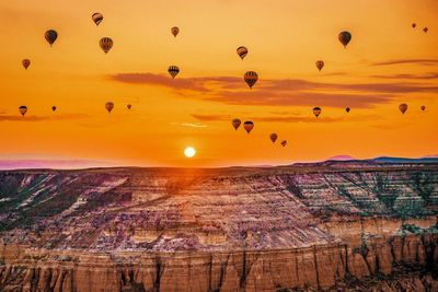 Low angle view of hot air balloons flying over landscape against sky during sunset