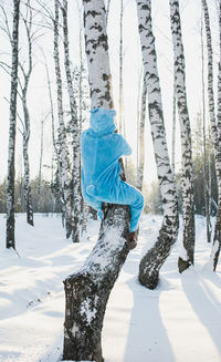 Rear view of mid adult man climbing tree in forest during winter
