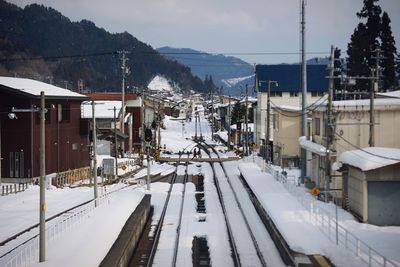 Snow covered railroad tracks by town against sky