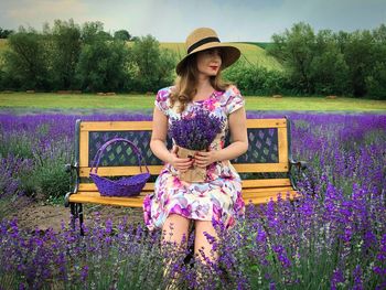 Young woman holding a bouquet of lavender sitting on a bench in a field of lavender