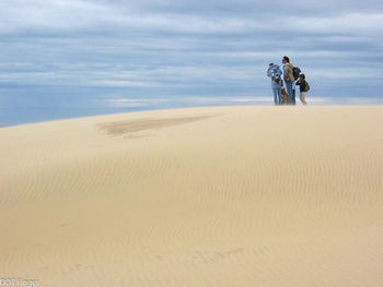 People standing on sand dune against cloudy sky