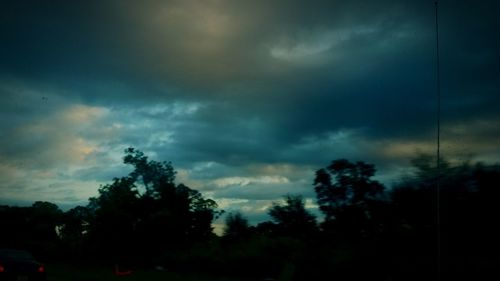 Silhouette trees against dramatic sky at dusk