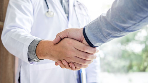 Midsection of doctor shaking hand with patient at hospital