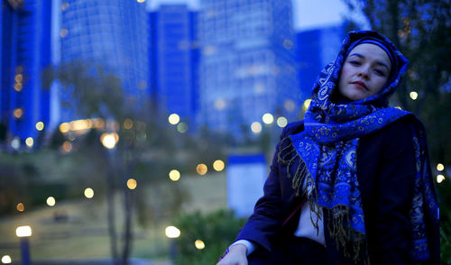 Portrait of young woman looking at illuminated city in winter