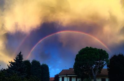 Low angle view of rainbow over trees against cloudy sky