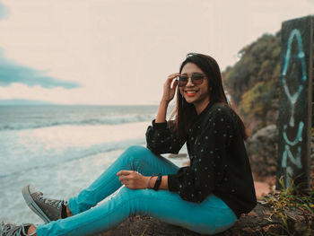 Young woman using mobile phone while sitting on beach