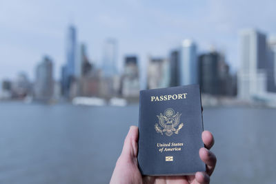 Cropped hand of person holding passport against buildings in city