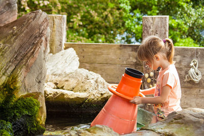 Side view of girl holding magnifying glass in pond