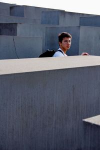 Portrait of young man looking away while standing against wall