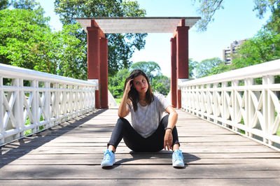 Full length of thoughtful young woman sitting on footbridge