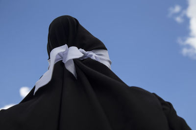 Low angle view of person in black traditional clothing against blue sky