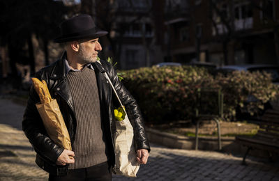 Adult man in hat holding bread and vegetable bag on street. madrid, spain