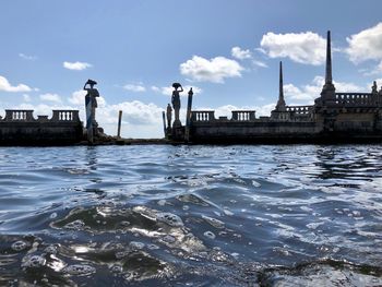 Statues by river against sky 