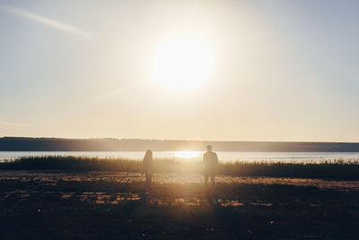 Silhouette people on beach against clear sky at sunset