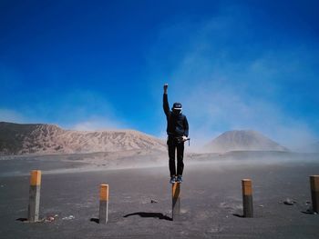 Full length of man standing on wooden post at desert against blue sky