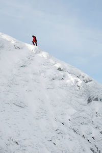 Low angle view of mountaineer climbing snowcapped mountain against sky