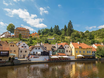 Houses by river and buildings in town against sky