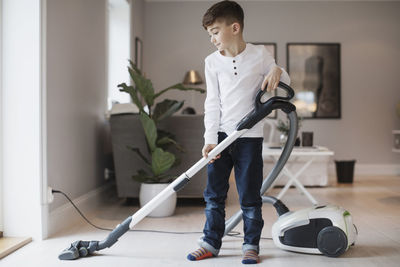 Boy using vacuum cleaner in living room at home