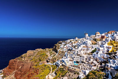 High angle view of townscape by sea against clear blue sky