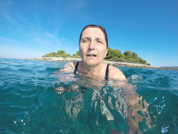 Portrait of woman swimming in sea against blue sky