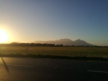 Road by field against clear sky during sunset