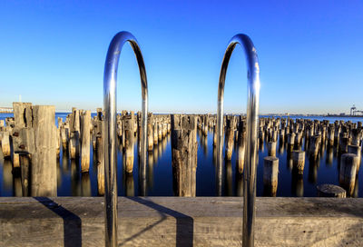 Wooden posts in sea against clear blue sky at princes pier