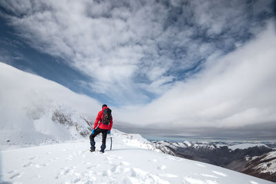 Rear view of man walking on snowcapped mountain against sky
