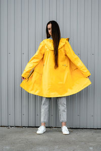 Girl in a yellow raincoat and gray jeans stands on a gray background. youth subculture