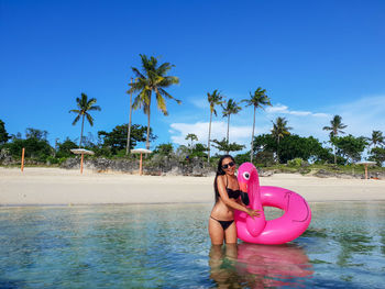 Portrait of young woman with inflatable ring standing in sea against blue sky