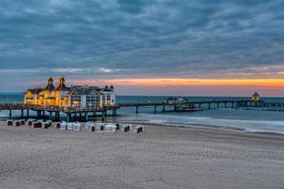 Pier on beach against sky during sunset