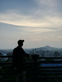 Silhouette man standing by railing against sky during sunset