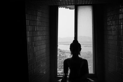 Scenic view of silhouette statue of the meditating buddha next to window