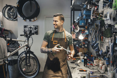 Smiling male mechanic looking at colleague while repairing pedal in workshop