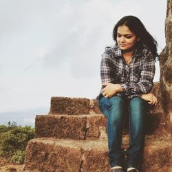 Young woman sitting on steps against sky