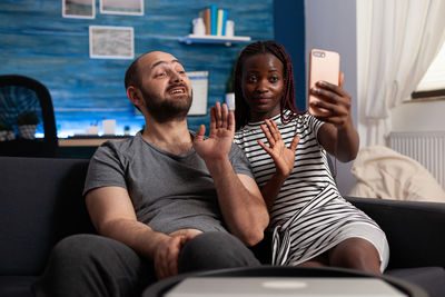 Couple talking on video call sitting on sofa at home