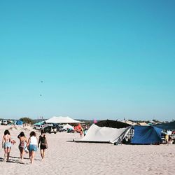 People at beach against clear blue sky