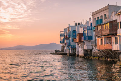 Buildings by sea against sky during sunset