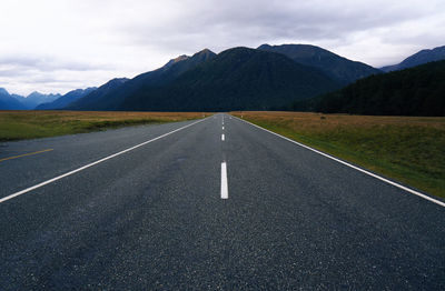 Country road leading towards mountains against sky