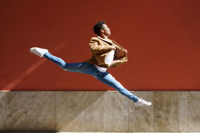 Side view of young man dancing against wall