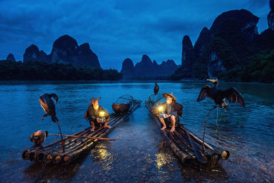 Men with illuminated lanterns sitting on wooden raft in lake